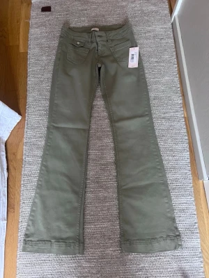 Olivgröna bootcut jeans - Snygga olivgröna bootcut jeans med klassisk femficksdesign och låg midja. Jeansen har en lätt utsvängd passform nertill och är tillverkade i ett mjukt bomullsmaterial. Perfekta för dig som gillar en avslappnad men trendig stil.