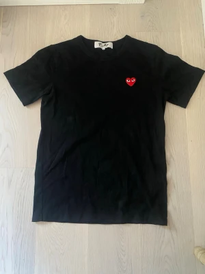 Comme des Garçons - Svart t-shirt från Comme des Garçons med det röda hjärtat med ögon broderat på bröstet. Storlek L men passar även M, använd fåtal gånger. Sååå snygg! 💕                                Nypris: 949 kr 