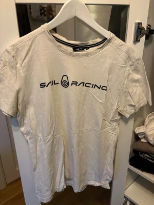 Vit t-shirt från Sail Racing - Vit t-shirt från Sail Racing med svart logga tryckt över bröstet . Inte använd mycket mest legad i garderoben. Skriv för frågor eller buda gärna 