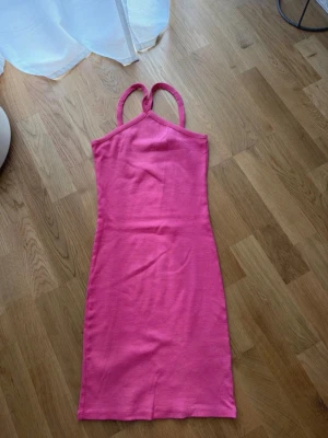 Rosa ribbad klänning från 157 - Säljer en rosa ribbad klänning från 157 med smala axelband som korsas i ryggen. Klänningen är figurnära och har en enkel, stilren design som passar perfekt till sommaren. Materialet är mjukt och stretchigt för en bekväm passform.