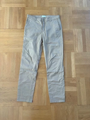 Beige chinos med rak passform - Snygga beige chinos med rak passform och klassiska fickor fram och bak. Byxorna har bälteshällor och stängs med dragkedja och knapp. Perfekta för en clean och stilren look. Materialet är mjukt och bekvämt, 98% bomull.