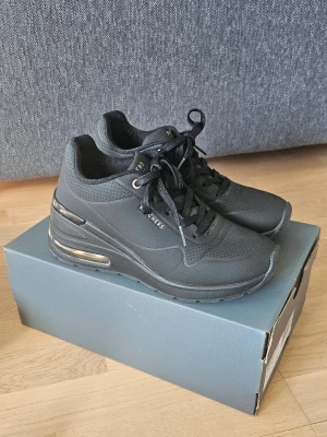 Svarta Skechers sneakers med luftkudde - Snygga svarta sneakers från Skechers med luftkudde i hälen och perforerat material på ovansidan. Skorna har svarta snören, diskreta detaljer i guld och en chunky sula som ger extra höjd. Perfekt för dig som gillar en sportig och modern look. Använda endast 2 gånger. 