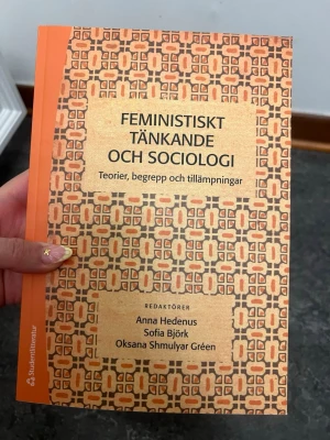 Feministiskt tänkande och sociologi - Kursbok med titeln 'Feministiskt tänkande och sociologi: Teorier, begrepp och tillämpningar', redaktörer Anna Hedenus, Sofia Björk och Oksana Shmulyar Gréen. Boken har ett mönstrat omslag i orange och beige toner och är tryckt i mjukpärm.