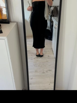 Svart tub långklänning  - Säljer en svart, tub långklänning med slits bak. Klänningen har en tight passform och är perfekt för dig som gillar en stilren och enkel look. Materialet känns mjukt och följsamt, troligen polyester eller bomull. Jätte snyggt med en kavaj över! ❤️