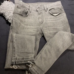 Levi's 512 flared jeans  - Snygga grå Levi's 512 jeans i slim fit med klassisk femficksdesign. Jeansen har råa, fransiga benslut för en cool och avslappnad vibe. Tillverkade i mjukt denim med en ljusgrå tvätt som ger en vintagekänsla. Perfekta för dig som gillar streetstyle.