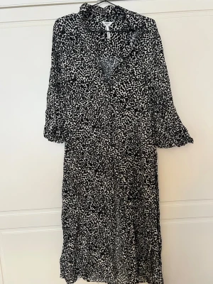 Svartvit mönstrad klänning Object - Svartvit långklänning från Object med leopardmönster. Klänningen har v-ringning och trekvartsärm med lätt volang vid ärmslut. Tillverkad i ett mjukt och följsamt material som ger en snygg siluett.