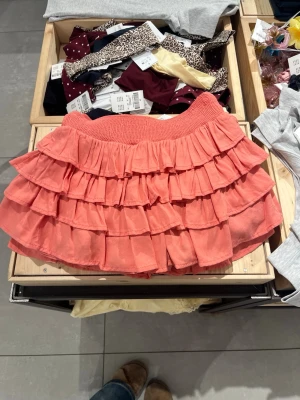 SÖKER💗 - Supersöt kort kjol i korallrosa med flera lager volanger och bred resår i midjan. Perfekt för dig som vill ha en lekfull och trendig look. Kjolen har en luftig känsla och passar till många olika stilar.