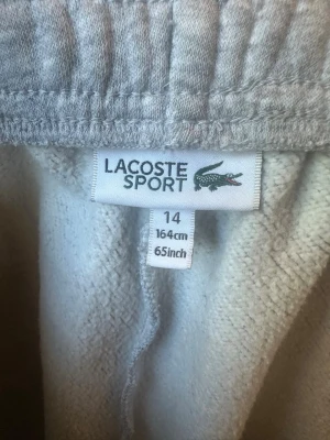  Lacoste grå mjukisbyxor från Lacoste Sport - Säljer ett par grå mjukisbyxor från Lacoste Sport med klassisk krokodil-logga på benet. Byxorna har resår i midjan med dragsko och muddar vid bensluten. Tillverkade i mjukt och bekvämt material, perfekta för chill dagar.