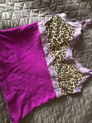Lila linne med leopard och spets - Linne i stark lila färg med leopardmönstrad byst och ljuslila spetsdetaljer. Justerbara axelband och mjukt, stretchigt tyg. Perfekt för dig som gillar djurmönster och färgkombinationer.