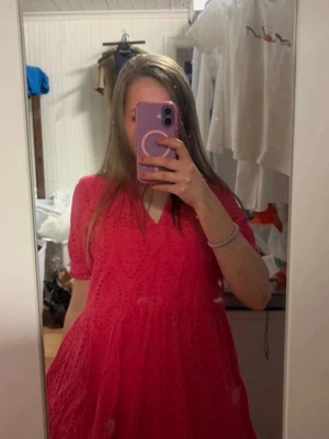 Rosa kortklänning från YAS - Supersöt rosa kortklänning från YAS i modellen Yasholi. Klänningen har v-ringning, volangdetaljer och korta ärmar. Tillverkad i ett lätt och luftigt material med broderade detaljer som ger en romantisk vibe.