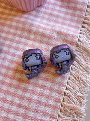 Två st Stranger Things Eddie upside down Funko Pop-figurer i metallic - Säljer två små Stranger Things kinder joy Eddie upside down Funko Pop-figurer med skimrande metallic-lila finish. Figurerna har stora huvuden, detaljerat hår och sitter i en avslappnad pose. Perfekta som samlarprylar eller dekoration till skrivbordet.