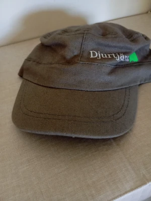 Brun keps från Djurtjänst AB - Säljer en brun keps från Djurtjänst AB med böjd skärm och broderad logga framtill. Kepsen är tillverkad i ett slitstarkt tyg och har en klassisk form som passar till många stilar.