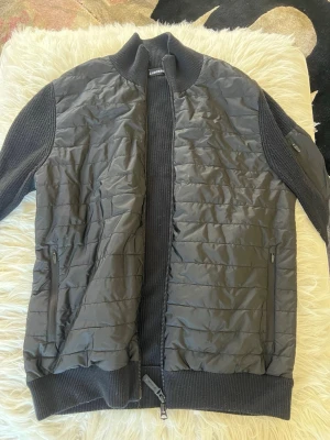 J Lindeberg Cardigan  - Snygg svart stickad cardigan från J Lindeberg. Passar perfekt till våren och hösten! Är använd och har lite sliten bomull på nedre ryggen, men det är lätt att fixa med rakhyvel.