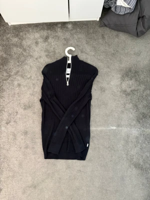 Mörkblå ribbstickad tröja Kronstadt - Snygg mörkblå ribbstickad tröja från Kronstadt med halv dragkedja vid halsen. Tröjan har lång ärm och hög krage, perfekt för lager på lager. Klassisk och stilren design som passar till mycket.