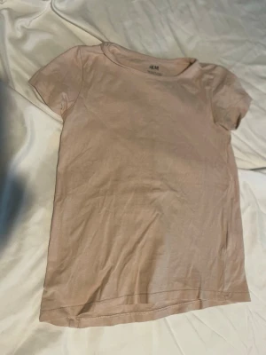 Ljusrosa t-shirt från H&M barn storlek 122/128 - En enkel och stilren ljusrosa t-shirt från H&M. T-shirten har rund halsringning och korta ärmar. Tillverkad i mjuk bomull. Perfekt basplagg att matcha med allt i garderoben. Barn storlek 122/128