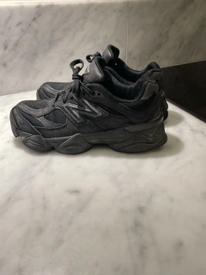 Svarta New Balance 9060 sneakers - Säljer ett par svarta New Balance 9060 sneakers med chunky sula och meshpaneler. Skorna har reflekterande detaljer och klassisk N-logga på sidan. Kombination av mocka och mesh ger en sportig och modern vibe. Perfekta för dig som gillar streetwear och stilrena sneakers.