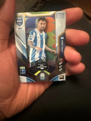 Panini FIFA 365 Adrenalyn samlarkort - Unikt Panini FIFA 365 Adrenalyn samlarkort med färgstark design och motiv från Road to FIFA World Cup. Kortet har detaljer i blått, vitt och guld samt officiell logga och kod på baksidan. Perfekt för samlare och fans av fotbollsspel.