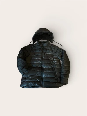 Svart quiltad dunjacka med huva - Snygg svart dunjacka med quiltad design och huva. Jackan har dragkedja framtill och långa ärmar. Perfekt för kalla dagar och har en klassisk, stilren look. Passar dig som vill ha en varm och lätt jacka med enkel passform.