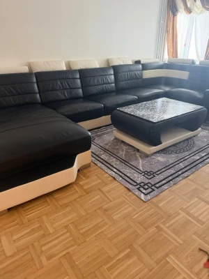 Sofforna - Bilden visar ingen kurslitteratur eller bok, utan ett vardagsrum med en svart och vit hörnsoffa och ett soffbord.