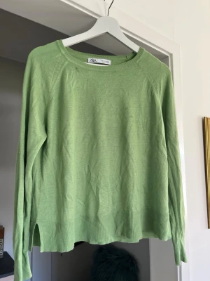 Grön stickad tröja från Zara - Ljusgrön stickad tröja från Zara med rund halsringning och långa ärmar. Tröjan har ribbade muddar vid ärmslut och nederkant samt små slitsar i sidorna. Perfekt för lager på lager och enkel att matcha med jeans eller kjol.