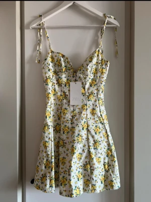 Blommig sommarklänning från ZARA - Söt kort klänning från ZARA med vita och gula blommor på ljus botten. Storlek XS och aldrig använd!!💛💛💛