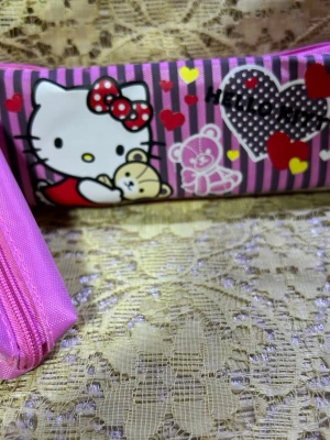 Hello Kitty rosa necessär - Söt necessär med Hello Kitty-motiv i rosa och lila ränder, dekorerad med hjärtan och nallebjörnar. Väskan har dragkedja och är gjord i slitstarkt syntetmaterial. Perfekt för småprylar eller smink.
