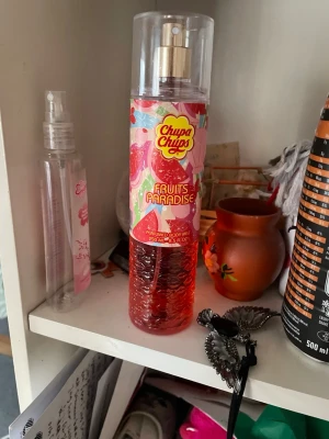 Chupa Chups Fruits Paradise Body Mist - Chupa Chups Fruits Paradise är en färgglad body mist med fruktig doft. Flaskan är genomskinlig med röd vätska och har ett lekfullt mönster i rosa, rött och grönt. Rymmer 250 ml och har en praktisk sprayfunktion. Perfekt för dig som gillar söta och fräscha dofter.