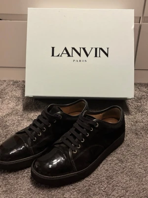 Lanvin’s svarta - Stilrena svarta sneakers från Lanvin med blank tå i lack och ovandel i mocka. Hel svarta i storlek 44. Allt original ingår! Låda, extra snören och dustbags. 100% äkta digitalt kvitto finns.