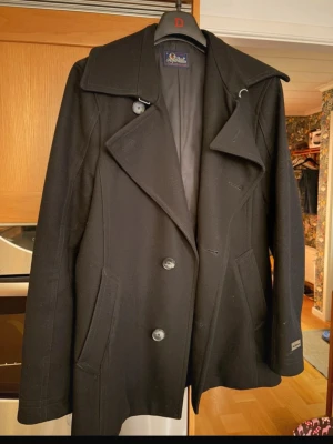 Snygg kappa herr - Stilren svart herrkappa från Peak Performance. Jacken är i ull och en snygg, stilren modell. Passar perfekt för att göra en outfit lite snyggare och vuxnare. 