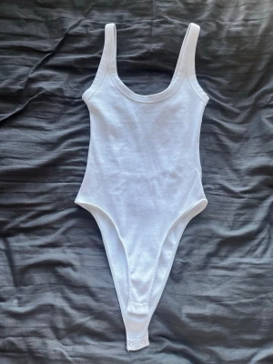 Vit basic body med breda axelband - Säljer en enkel och stilren vit body med breda axelband och rundad urringning. Bodyn har hög skärning vid benen och knäppning i grenen. Tillverkad i mjukt bomullsliknande material som känns bekvämt mot huden. Perfekt att styla till jeans eller kjol. Säljer då jag aldrig använt den och känner att någon annan troligtvis har bättre användning av den💘