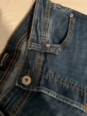 Blå jeans från Jack & Jones - Säljer ett par klassiska blå jeans från Jack & Jones med snygga kontrastsömmar och femficksmodell. Jeansen har normal midja och rak passform, tillverkade i slitstark denim. Perfekta för en avslappnad och trendig look.
