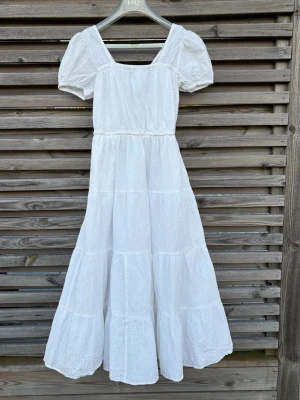 Vit lång klänning med puffärm - Säljer denna ljuvliga vita sommarklänning som jag själv köpte på Sellpy i "mycket bra skick". Tyvärr var den lite för stor för mig, så den förtjänar ett nytt hem där den kommer till användning!  • Stil: Romantisk klänning med puffärm och våningas-kjol (tiered skirt). • Detaljer: Vacker öppen rygg med två nätta knytband och markerad midja med resår. • Material: Tyget har en fin struktur (likt bäckebölja) som ger klänningen liv och gör den nästintill strykfri. • Skick: Mycket gott skick. 