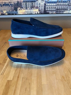 Marinblå mocka loafers från Luis Ricardo - Snygga marinblå loafers i mocka från Luis Ricardo. Skorna har en klassisk slip-on design med rundad tå och vit sula som ger en fräsch kontrast. Perfekta för dig som vill ha en stilren och modern look till vardagsoutfiten.