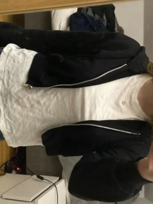 Svart hoodie med dragkedja - Säljer en svart hoodie med dragkedja framtill och huva. Hoodien har en avslappnad passform och är perfekt att slänga på sig över en t-shirt. Passar till jeans eller mjukisbyxor för en chill look.