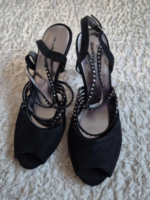 Svarta pumps med strass från Graceland - Säljer ett par svarta pumps från Graceland med öppen tå och flera tunna remmar dekorerade med strass. Skorna har en elegant design med klack och mjuk sammetsliknande yta. Perfekta för dig som vill ha något extra till outfiten.