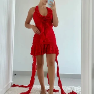 Röd volangklänning med snörning - Supersnygg röd kortklänning med volanger och djup v-ringning. Klänningen har snörning i halsen och långa band som hänger ner, samt flera lager volanger i kjolen. Perfekt för dig som vill sticka ut och älskar statement-plagg. Bilden är lånat!