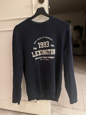 Mörkblå Lexington sweatshirt - Mörkblå sweatshirt från Lexington med tryck framtill i vitt med texten '1993 Lexington American Original Heritage'. Rund halsringning och ribbade muddar vid ärmslut och nederkant. Perfekt för en avslappnad och stilren look.