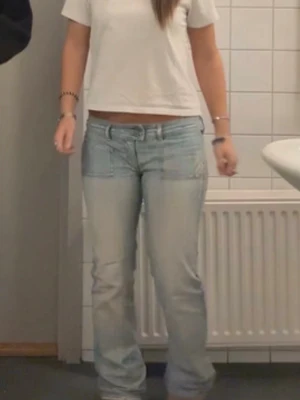 Ljusblå Diesel  low waist jeans  - Säljer ett par ljusblå low waist jeans med tydliga patchdetaljer över höfterna och raka ben. Jeansen har klassisk femficksmodell och är tillverkade i denim med en avslappnad passform. Perfekta för en trendig och avslappnad stil.