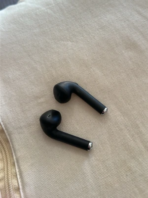 Svarta trådlösa in-ear hörlurar - Säljer ett par stilrena svarta trådlösa in-ear hörlurar med slimmad design och silverdetaljer i ändarna. Perfekta för musik, poddar eller samtal på språng. Passar både iPhone och Android via Bluetooth.