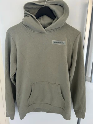 Grön hoodie från Peak Performance - Snygg grön hoodie från Peak Performance med broderad logga på bröstet. Klassisk känguruficka framtill och mjukt material som känns skönt mot huden. Perfekt för dig som gillar en clean och stilren look. Huva med dragsko för extra komfort.