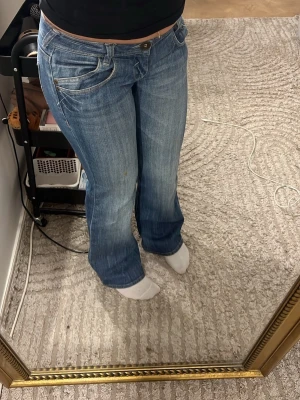 Blå bootcut jeans med låg midja - Säljer ett par blå vintage bootcut jeans med låg midja och snygga slitningar. Köpt saconahand