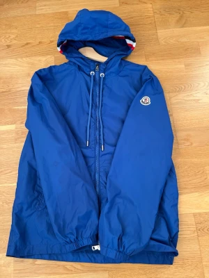 Moncler vindjacka - Snygg blå vindjacka från Moncler med huva och dragkedja 🧥Perfekt för vindiga dagar samt våren 🍃Dragkedjan är lite trög och NFC-tagg finns självfallet ⛓️‍💥 Passar perfekt för dig som är 164-170cm +/-🧍‍♂️