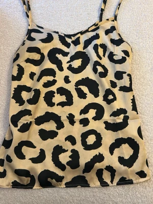 Leopardmönstrad linnetopp - Snygg linnetopp med leopardmönster i beige och svart. Tunn och lätt med smala axelband och rak passform. Perfekt för dig som vill sticka ut med ett djurmönstrat plagg.