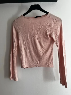 Ljusrosa långärmad topp - En enkel och stilren ljusrosa långärmad topp i mjuk bomull. Modellen är rak med rund halsringning och har en croppad passform som passar perfekt till både jeans och kjol. Perfekt basplagg för din garderob. Använd ca 1 gång