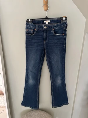 Blå bootcut jeans med fickor - Snygga blå bootcut jeans med klassisk femficksdesign och lätt slitna detaljer på framsidan. Jeansen har normal midja och är tillverkade i ett mjukt denimtyg som ger en bekväm passform. Perfekta för en avslappnad och trendig look.