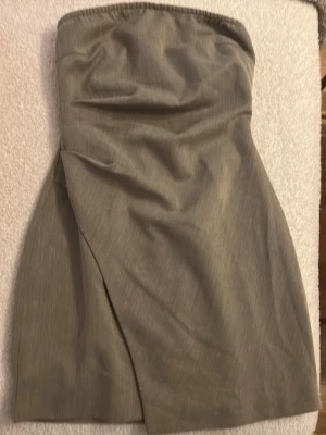 Beige axelbandslös kort klänning - Snygg beige axelbandslös klänning med omlott-detalj framtill. Klänningen har en enkel och stilren design, perfekt för dig som gillar minimalistiskt mode. Materialet känns som en blandning av bomull och polyester och modellen är figurnära.