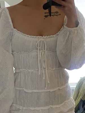 Vit kort klänning  - Söt vit kort klänning med puffiga långärmar, broderade blommor och volangdetaljer. Klänningen har snörning framtill och elastisk midja för en bekväm passform. Perfekt för sommarens alla tillfällen. Passar mig som har xs/s 