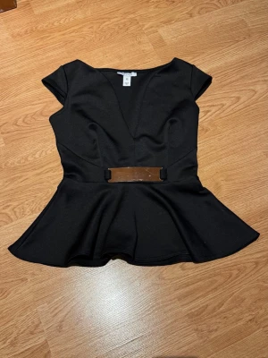 Svart peplum topp med bälte - Svart peplum topp med v-ringning och metallbälte. Har aldrig använt den då den är för liten. Den har en liten repa på bältet, inget som syns💕