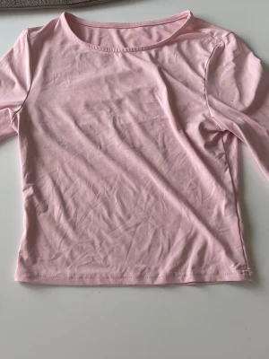 Ljusrosa långärmad topp - En enkel och stilren ljusrosa långärmad topp med rund halsringning. Tillverkad i mjukt material som känns skönt mot huden. Perfekt att matcha med jeans eller kjol för en avslappnad look.