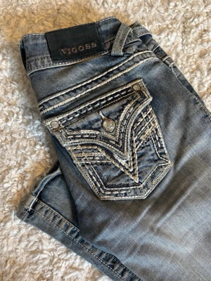 Blå jeans med broderade fickor - Snygga blå jeans från Vigoss med unika broderade detaljer på bakfickorna och kontrastsömmar. Tyvärr sönder vid grenen och fickan men går att laga. Köptes på A2 vintage för 700 kr. Mått; Midja: 36cm. Längd 100cm. Innerbenslängd: 80cm. Gren 18cm